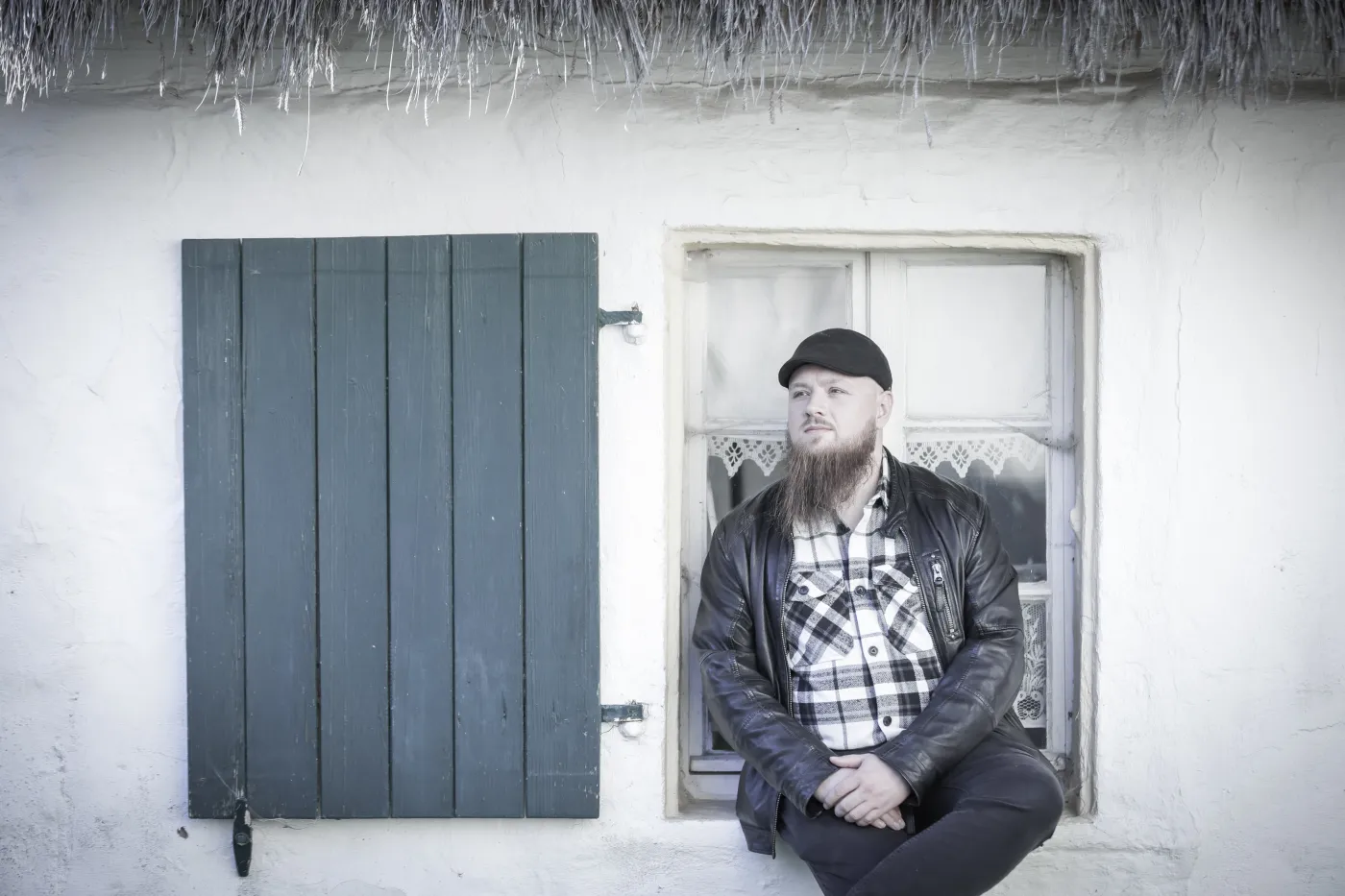 Nico Schwappacher (Zwischenlichten) sitzt lässig im Rahmen eines alten Fensters. Links von ihm ist ein großer Fensterladen zu sehen. 